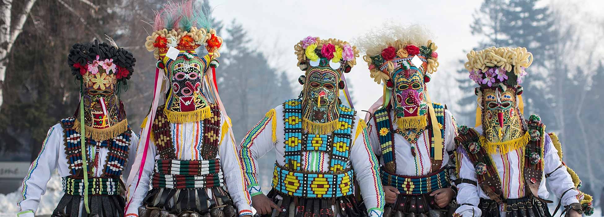 Grupo de cinco personas con elaborados trajes y máscaras tradicionales de Kukeri búlgaros.